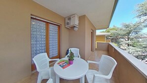 A balcony with a table, chairs, a potted plant, and an air conditioning unit. - Equipped Flat for a Comfy Family Stay (Lignano Sabbiadoro)