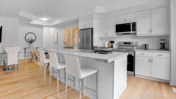 Una cocina moderna con armarios blancos, electrodomésticos de acero inoxidable y una isla central con taburetes de bar.