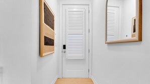 Un pasillo con una puerta blanca, un espejo y una rejilla de ventilación.
