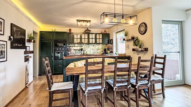 Un coin repas avec une table et des chaises en bois, une cuisine avec des meubles verts et une horloge au mur.