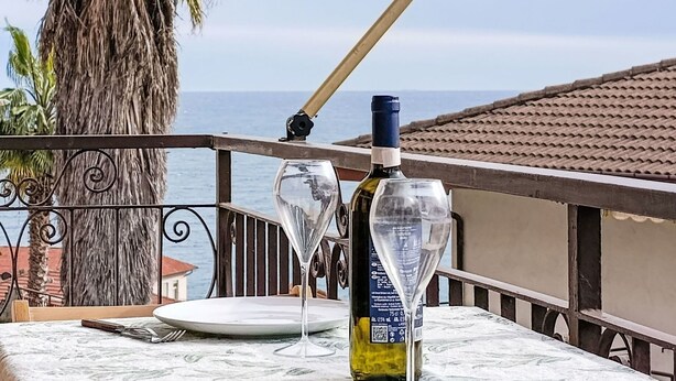A table with a wine bottle, a glass, and a fork on a balcony overlooking the sea. - Lovely apartment for 4 guests with pool, A/C, WIFI and balcony (Cipressa)