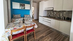 A compact living space with a dining area, kitchenette, and a blue accent wall. - Lovely apartment for 4 guests with pool, A/C, WIFI and balcony (Cipressa)