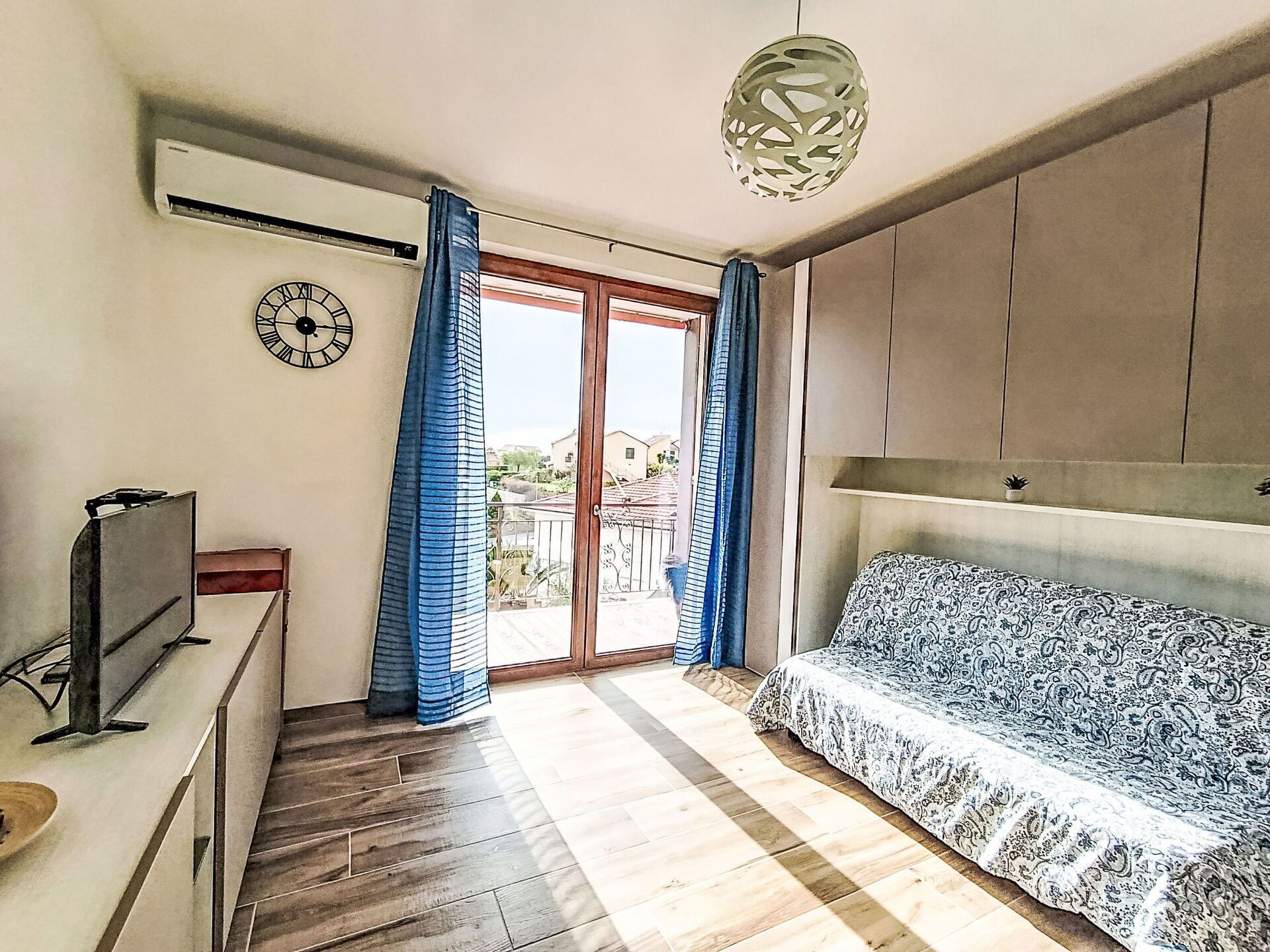Ein Zimmer mit einer Couch, einem Fernseher, einer Uhr und einem Fenster mit Vorhängen.