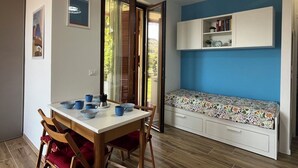 A dining area with a table set for two, a bench with a floral cushion, and a white cabinet above. - Lovely apartment for 4 guests with pool, A/C, WIFI and balcony (Cipressa)