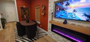 A modern living room with a fireplace, a TV, and a dining area. - Downtown Tuk Tuk Social House with Photo booths , Hot Tub, Sauna and a Gym (Houston)