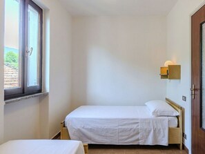 Ein kleines, sauberes Zimmer mit zwei Einzelbetten, einem Fenster und einer Wandleuchte.