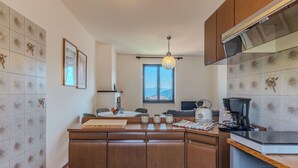 A compact kitchen with a central island, a dining area, and a view through a window. - Nice apartment for 4 people with WIFI, TV, balcony and pets allowed (Peglio)