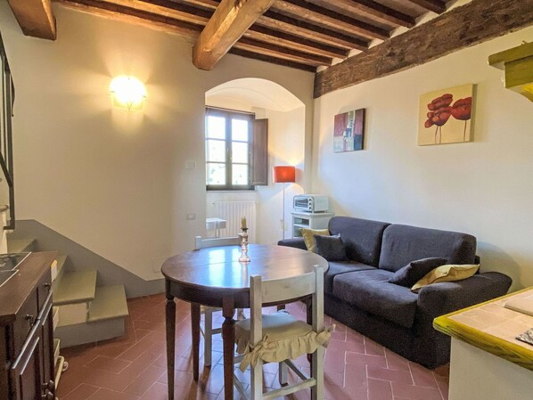 Un coin repas avec une table ronde et des chaises, un canapé, un radiateur et une fenêtre donnant sur un beau paysage.