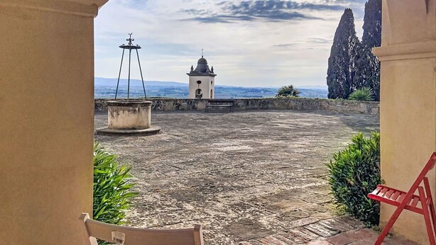 Ein Innenhof mit einem Brunnen, einem kleinen Turm und einer Bank.