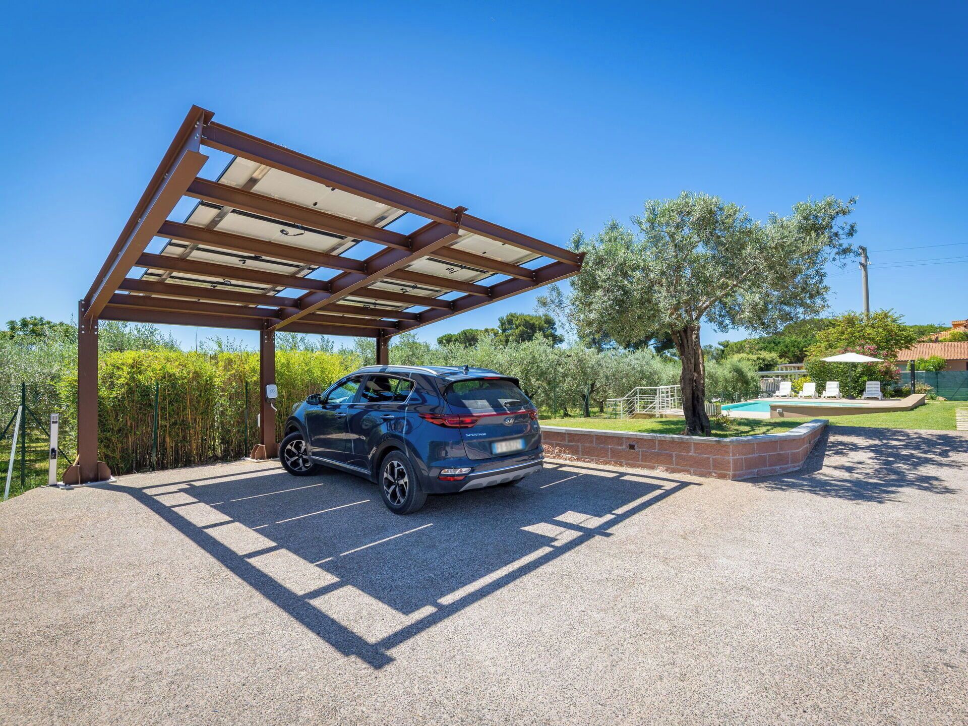 Un'area di parcheggio con un carport coperto, una piscina e un giardino curato.