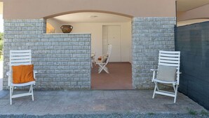 Eine Terrasse mit zwei weißen Stühlen, einem Tisch und einer dekorativen Vase.