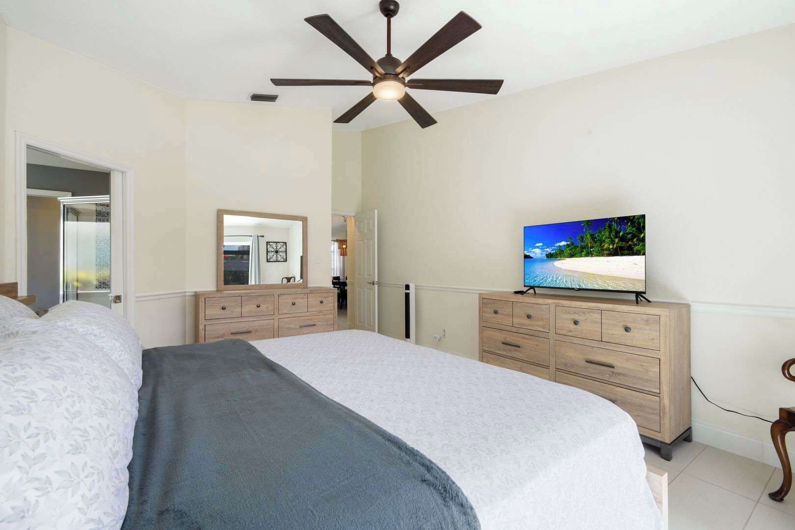 A bedroom with a bed, a dresser, a television, a ceiling fan, and a mirror.
