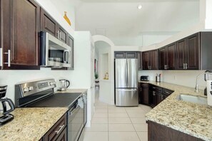 A modern kitchen with dark wood cabinets, stainless steel appliances, granite countertops, and a central island. - Villa Bluegarden- a slice of paradise (Cape Coral)