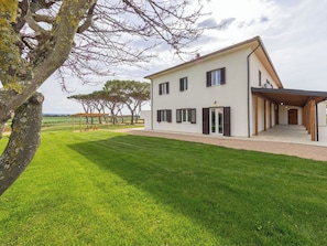 Ein zweistöckiges Haus mit überdachter Terrasse, Rasenfläche und Blick auf die Landschaft.