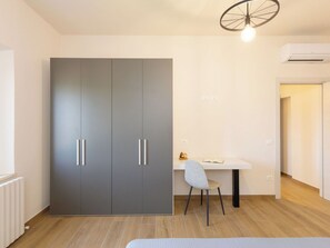 Ein modernes Zimmer mit einem grauen Wandschrank, einem kleinen Schreibtisch mit Stuhl und einem Heizkörper.