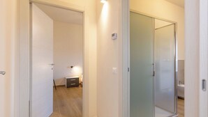 Um corredor com piso de madeira, uma porta de vidro deslizante e uma pequena mesa de cabeceira com abajur.