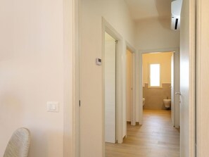 Ein Flur mit einer zur Toilette führenden Tür, einer Decken-Klimaanlage und einem Fenster, das für natürliches Licht sorgt.