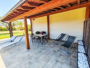 Eine Terrasse im Freien mit Tisch und Stühlen, zwei Liegestühlen und einer Pergola.