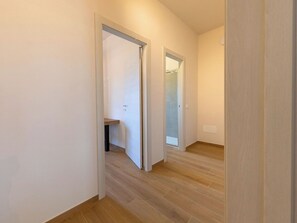 Ein Flur mit Holzboden, weißen Wänden und einer Tür zu einem Badezimmer mit Duschabtrennung aus Glas.