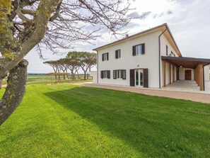 Ein zweistöckiges Haus mit überdachter Terrasse, Rasenfläche und Blick auf die Landschaft.