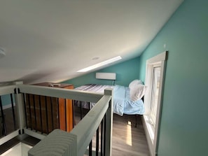 Une chambre à coucher avec un lit, une table de chevet, une fenêtre et un escalier.