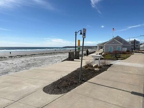 Une promenade en bord de mer avec un banc, une tour de surveillance pour les sauveteurs et un bâtiment sur lequel flotte un drapeau.