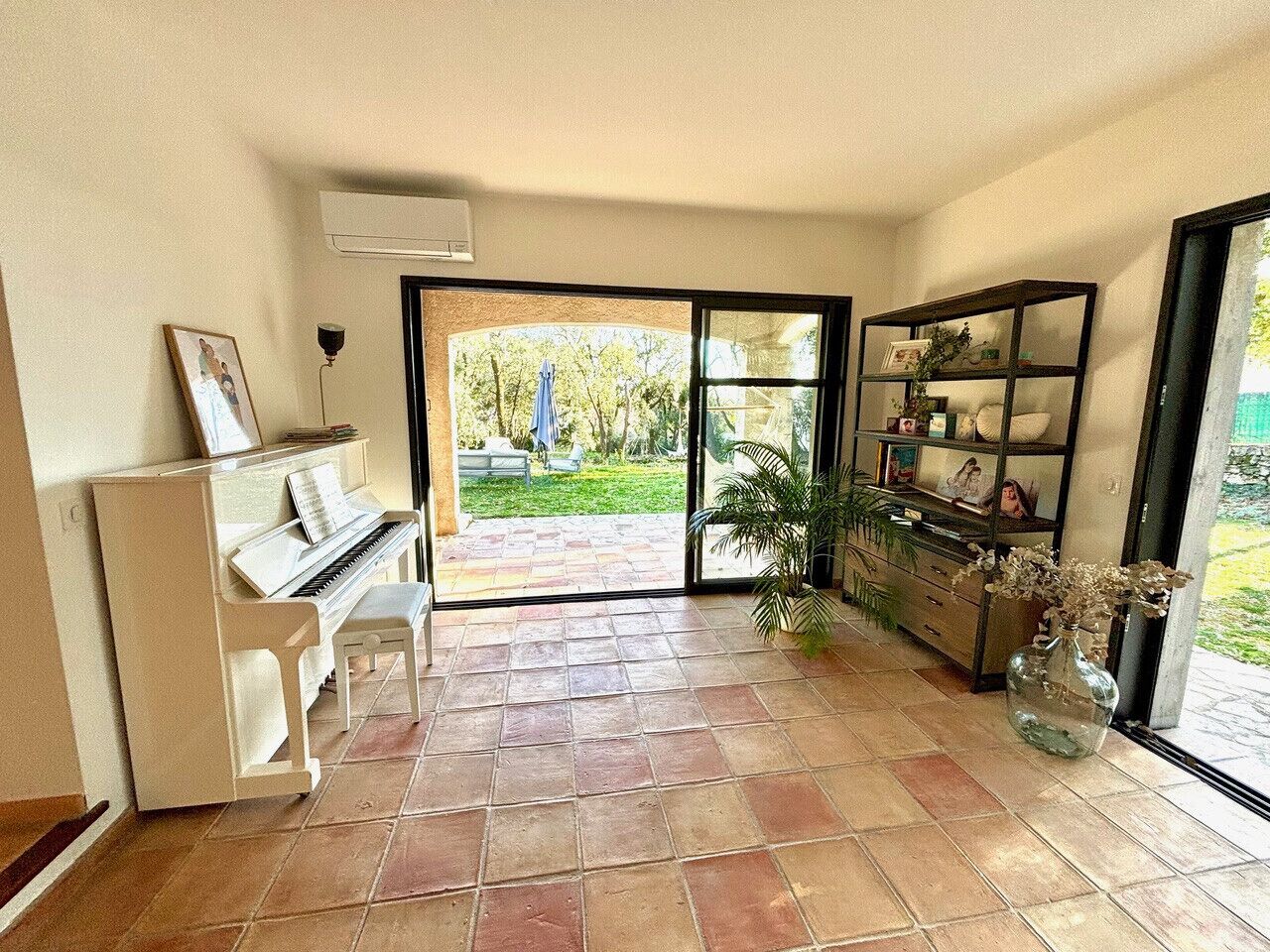 A living room with a piano, a bookshelf, and a large window.