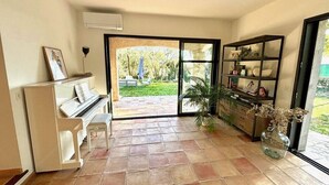 Una sala de estar con un piano, una estantería y un ventanal grande.