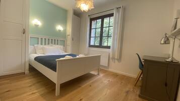 A bedroom with a bed, a desk, a chair, a window, and a hanging light fixture.