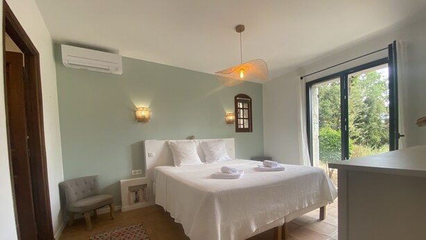 Un dormitorio con una cama, una silla, una mesita, un ventanal y una puerta.