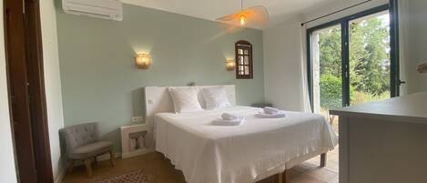 A bedroom with a bed, a chair, a small table, a window, and a door.