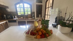 Una cocina con un frutero en la encimera, una botella de aceite de oliva, una bolsa de aperitivos y una planta en maceta.