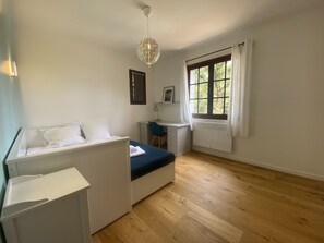 Une chambre à coucher comprenant un lit, un bureau, une chaise, une fenêtre avec des rideaux et un luminaire suspendu.
