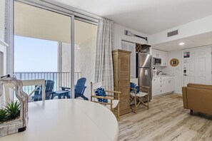 A modern living room with a dining table, chairs, a sofa, and a kitchen area with a refrigerator and cabinets. - Beachfront Condo, King Bed + Bunks | Sleeps 4 | Balcony Gulf Views | Long Beach Resort Tower 1 (Panama City Beach)
