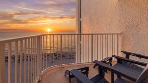 En balkon med udsigt til solnedgangen over havet, træbænke og en struktureret væg.
