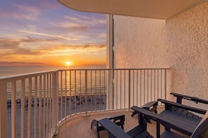 A balcony with a view of the sunset over the ocean, wooden benches, and a textured wall. - Beachfront Condo, King Bed + Bunks | Sleeps 4 | Balcony Gulf Views | Long Beach Resort Tower 1 (Panama City Beach)