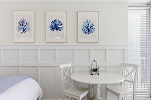 A hotel room with a bed, a round table with chairs, and three framed blue leaf artworks on the wall. - Beachfront Condo, King Bed + Bunks | Sleeps 4 | Balcony Gulf Views | Long Beach Resort Tower 1 (Panama City Beach)