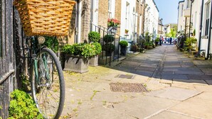 A narrow street with a bicycle parked on the left, a wicker basket attached to the bike, and a row of buildings on both sides. - 1Bed Central Apt With Parking! (Cambridgeshire)