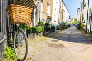 A narrow street with a bicycle parked on the left, a wicker basket attached to the bike, and a row of buildings on both sides. - 1Bed Central Apt With Parking! (Cambridgeshire)