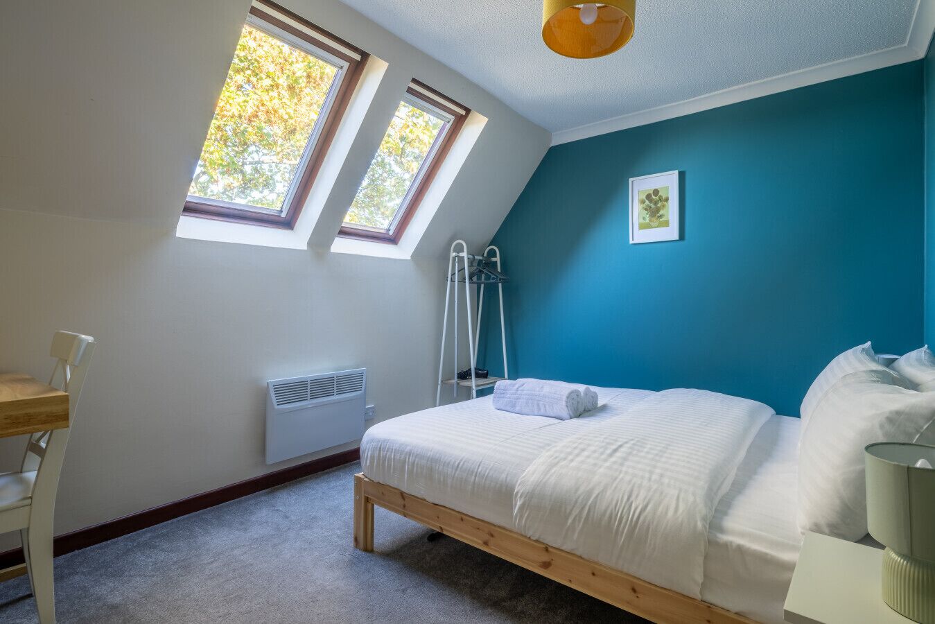 Une chambre avec un puits de lumière, un lit, un radiateur, un bureau et une chaise.