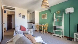 A cozy living room with a sofa, a dining table with chairs, a bookshelf, and a kitchen in the background. - 1Bed Central Apt With Parking! (Cambridgeshire)