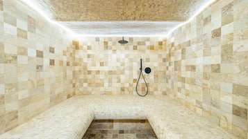 A spa room with mosaic tiled walls and floor, a bench, and a showerhead.
