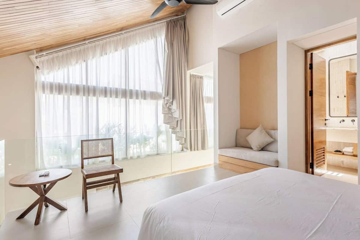A hotel room with a bed, a chair, a small table, a sofa, and a view of a staircase.