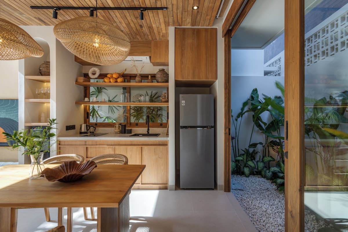 A modern kitchen with wooden cabinets, a stainless steel refrigerator, and a dining area with a wooden table and chairs.