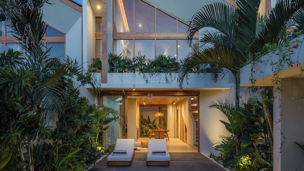 A modern house with a pool, lounge chairs, and tropical plants.