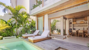 A modern outdoor pool area with lounge chairs, a wooden deck, and lush tropical plants.