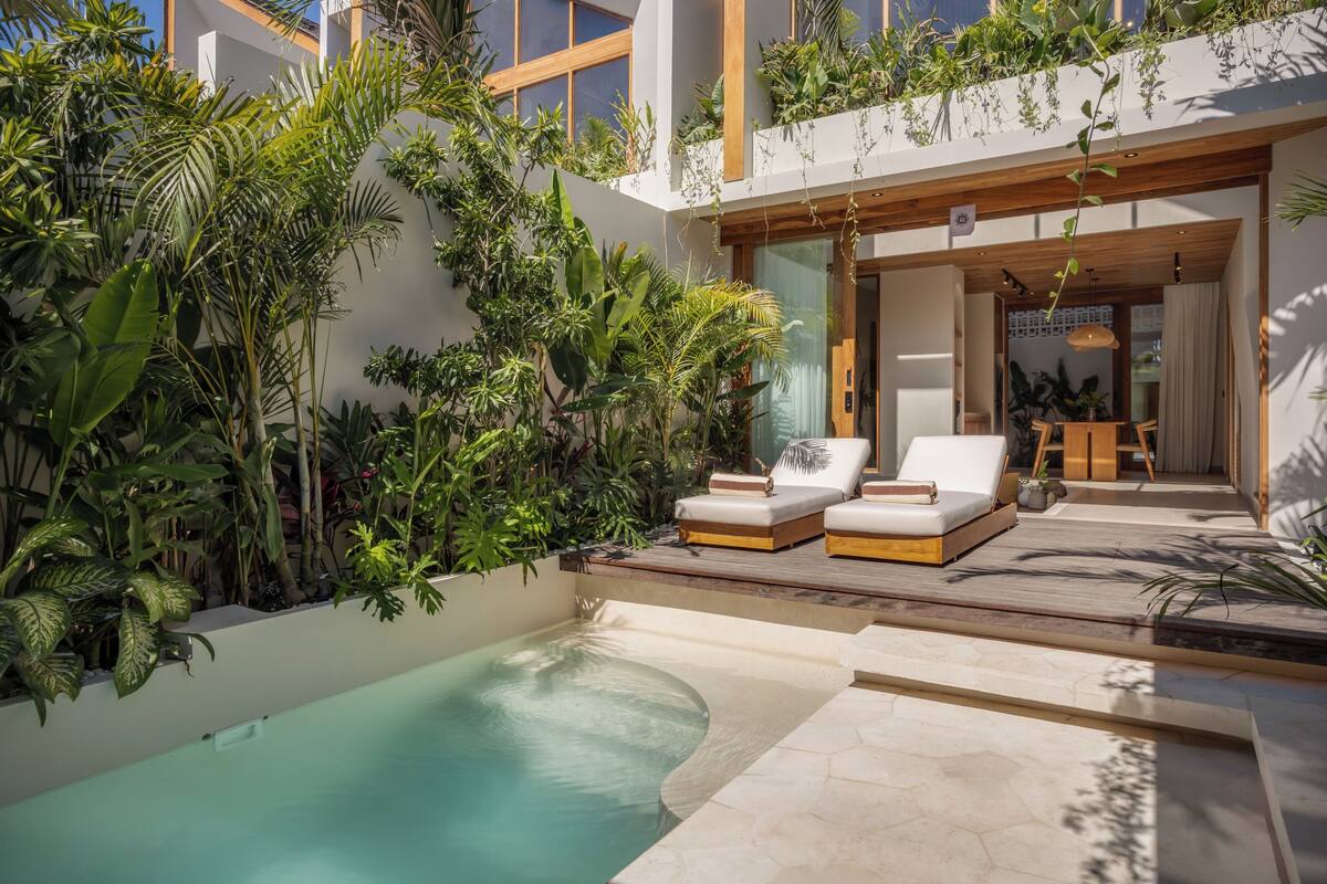 A poolside area with lounge chairs, a wooden deck, and lush greenery.