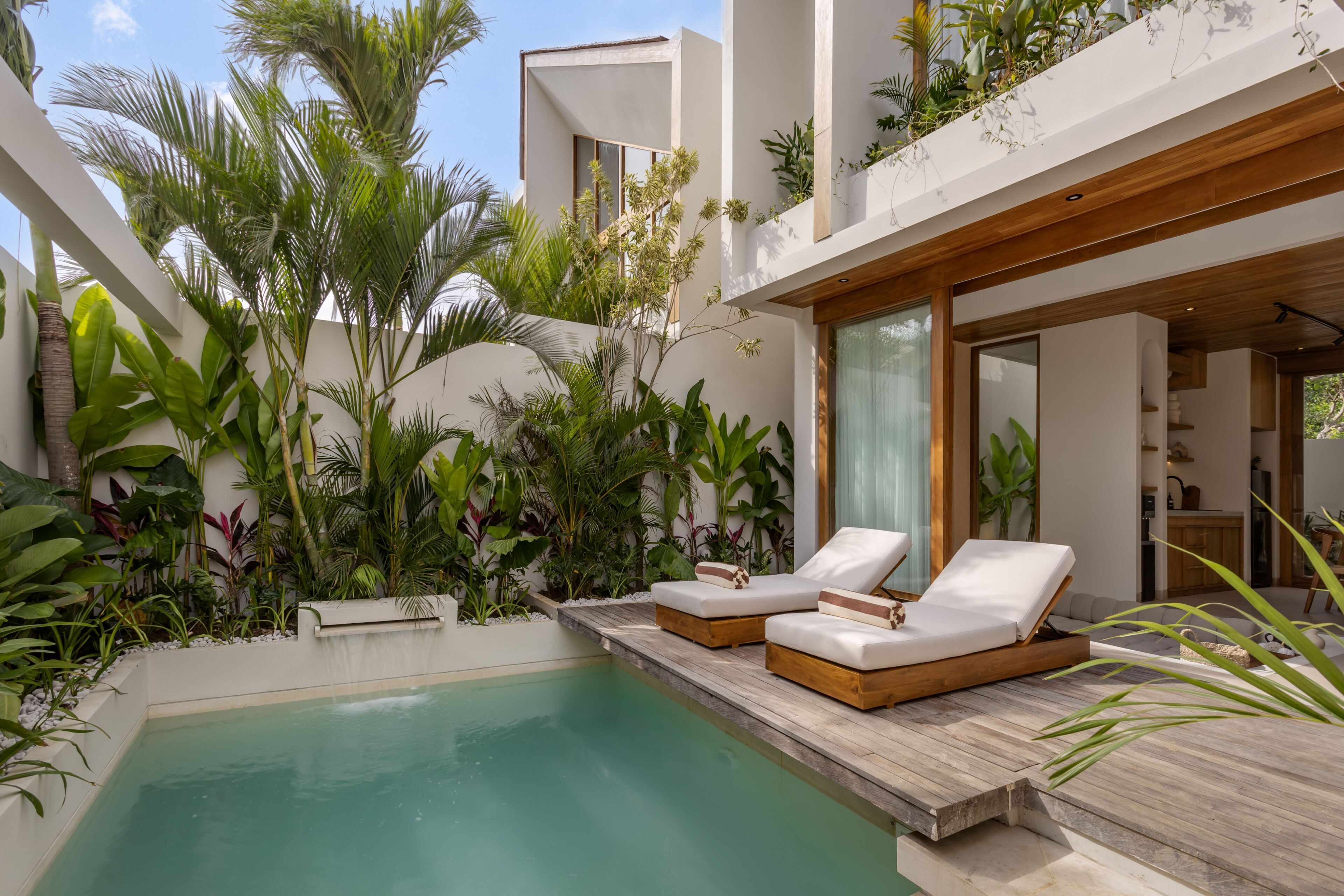 A modern pool area with lounge chairs and lush tropical plants.