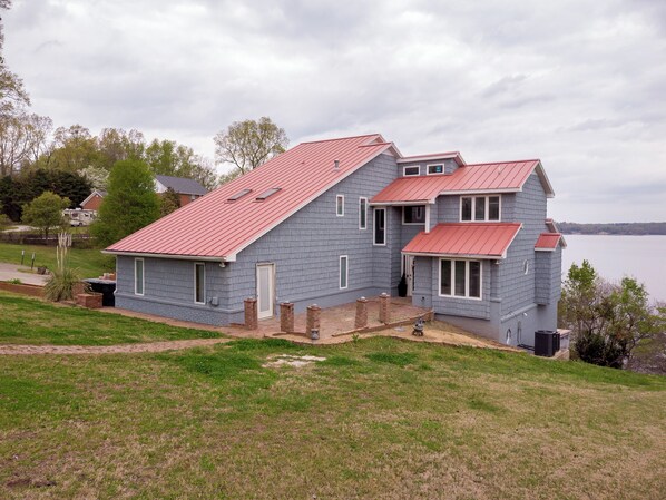 A two-story house with a red roof, a front porch, and a view of a body of water.