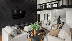 Ein modernes Wohnzimmer mit Kamin, Flachbildfernseher und einer Treppe, die in ein Obergeschoss führt.